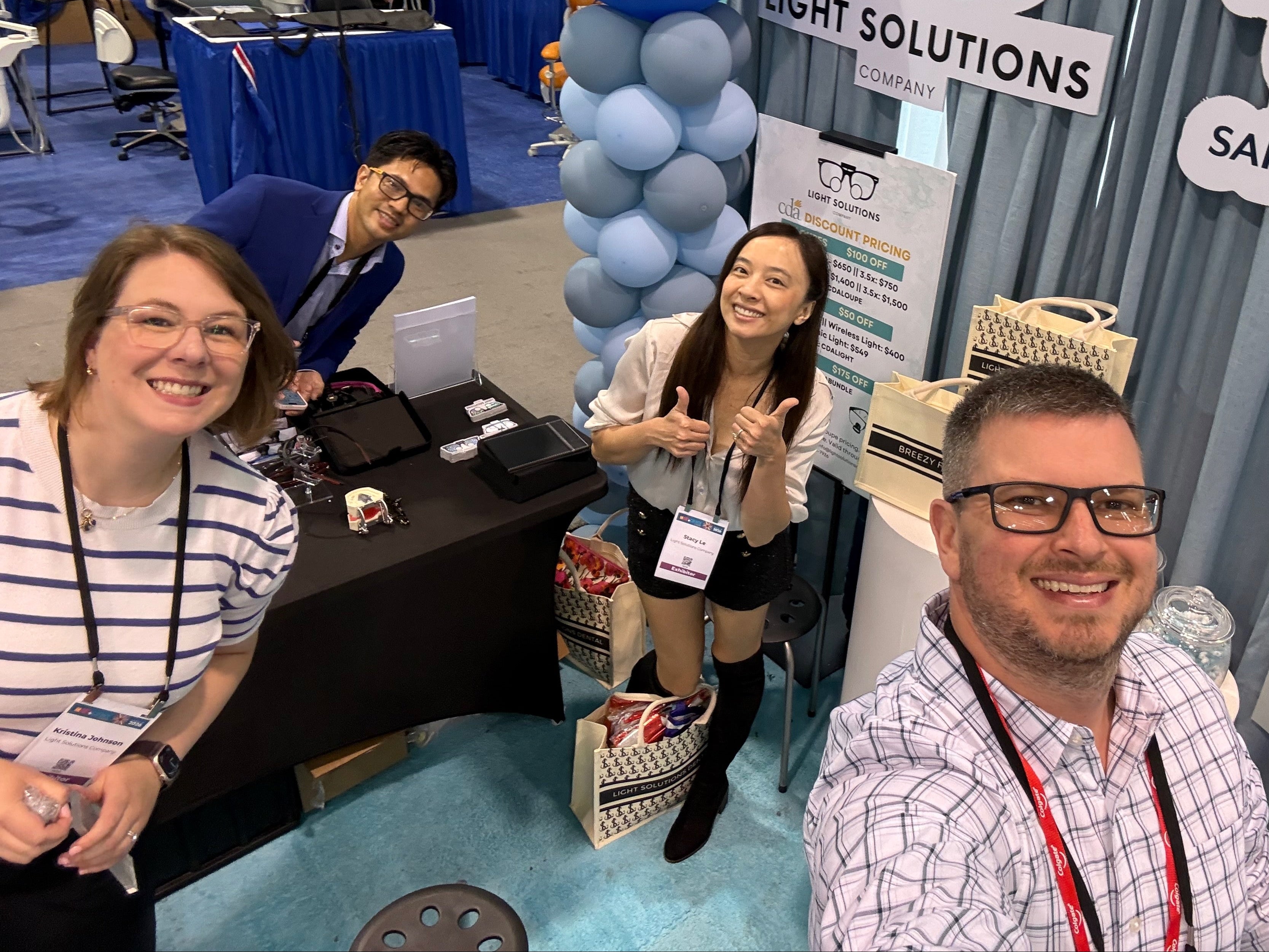 The founders, Kristina, Thanh, Stacy, and Matt, at a convention or trade show with booths and balloons.